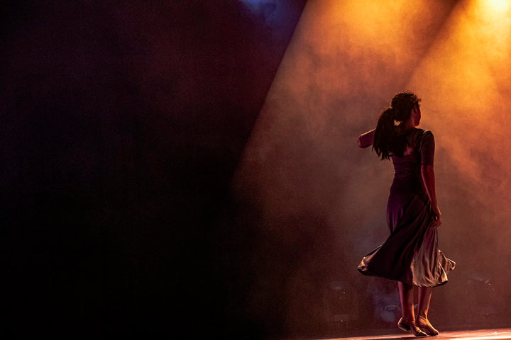 A woman in a dark dress dancing on stage under warm orange light — illustrative stock photo