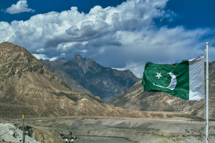 a pakistan flag flying in front of a mountain range — illustrative stock photo